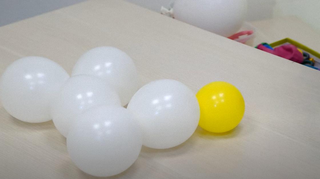 На столе лежат наполненные воздухом маленькие белые шарики и один желтый