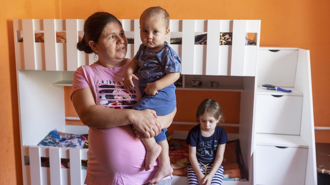 Беременная женщина стоит с ребенком на руках в комнате