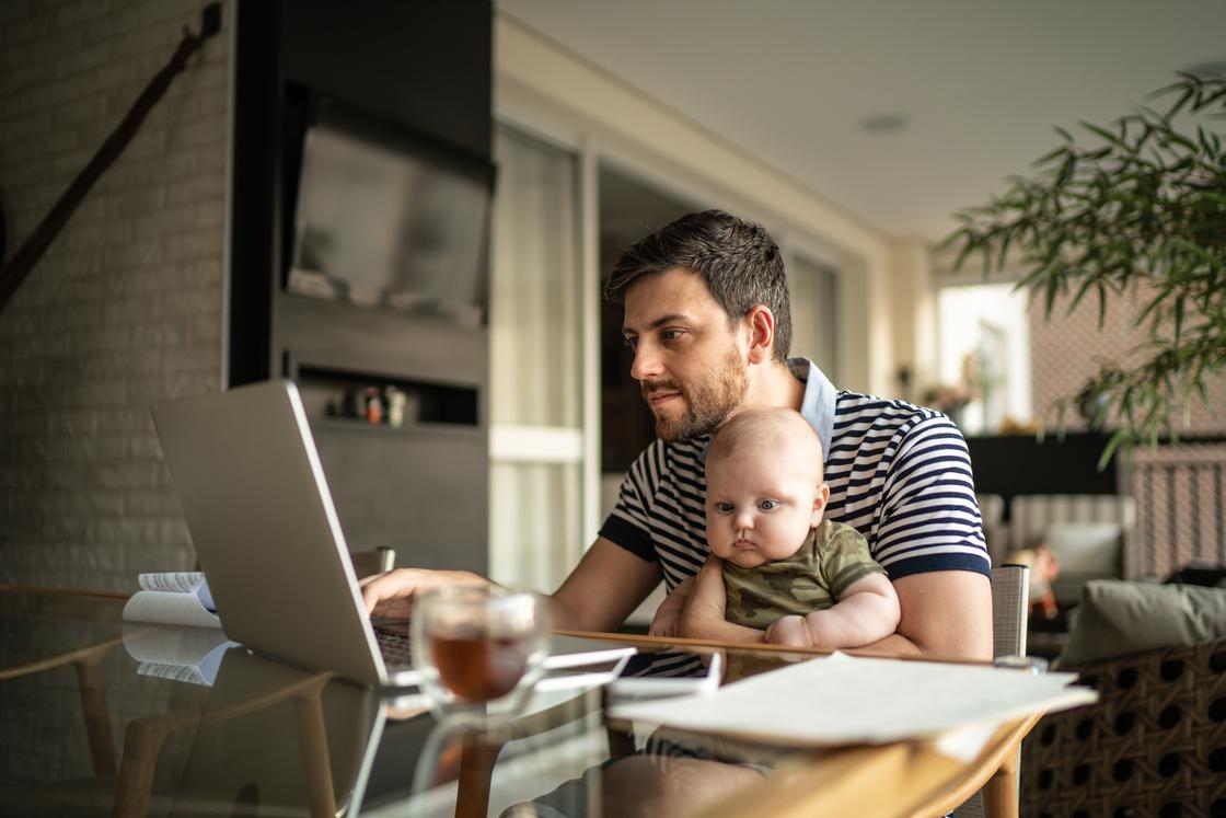 Мужчина работает за компьютером с ребенком на руках