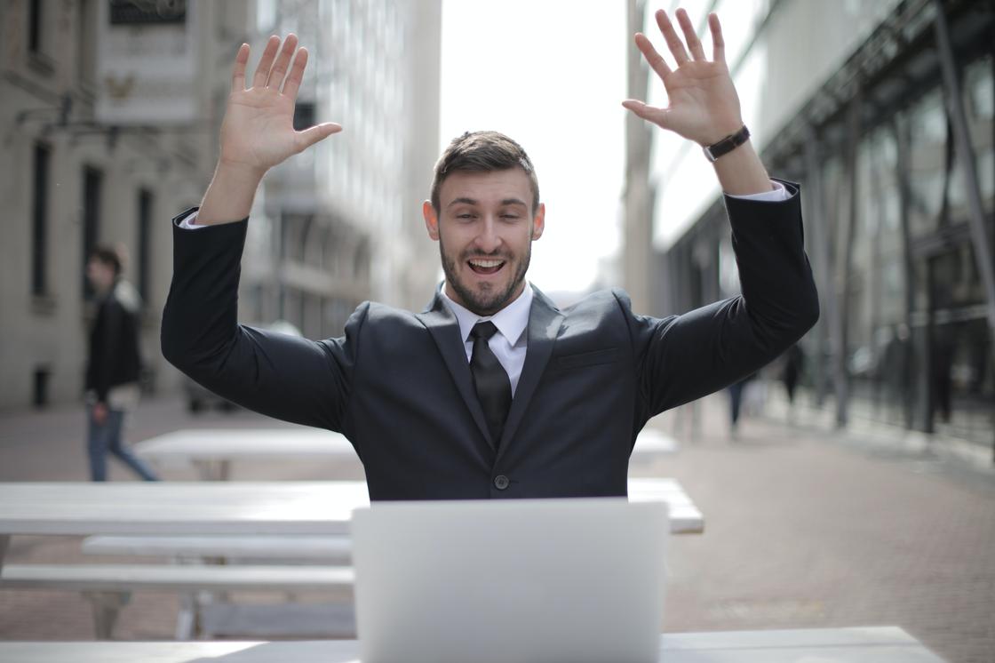 Радостный мужчина в костюме смотрит на монитор ноутбука