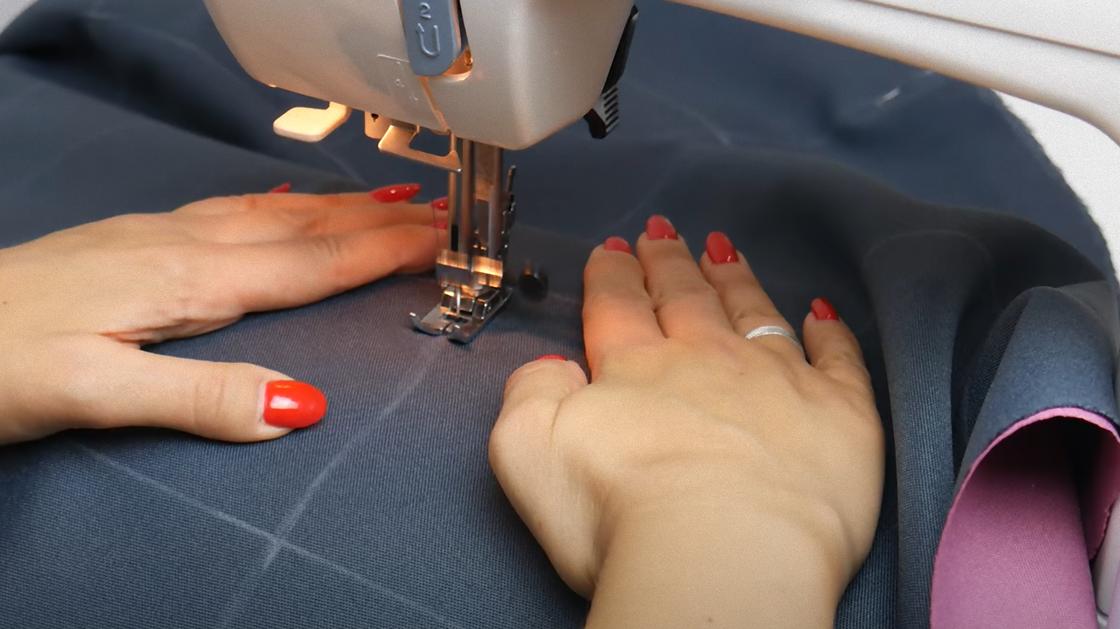 На швейной машинке делают строчку по серой ткани