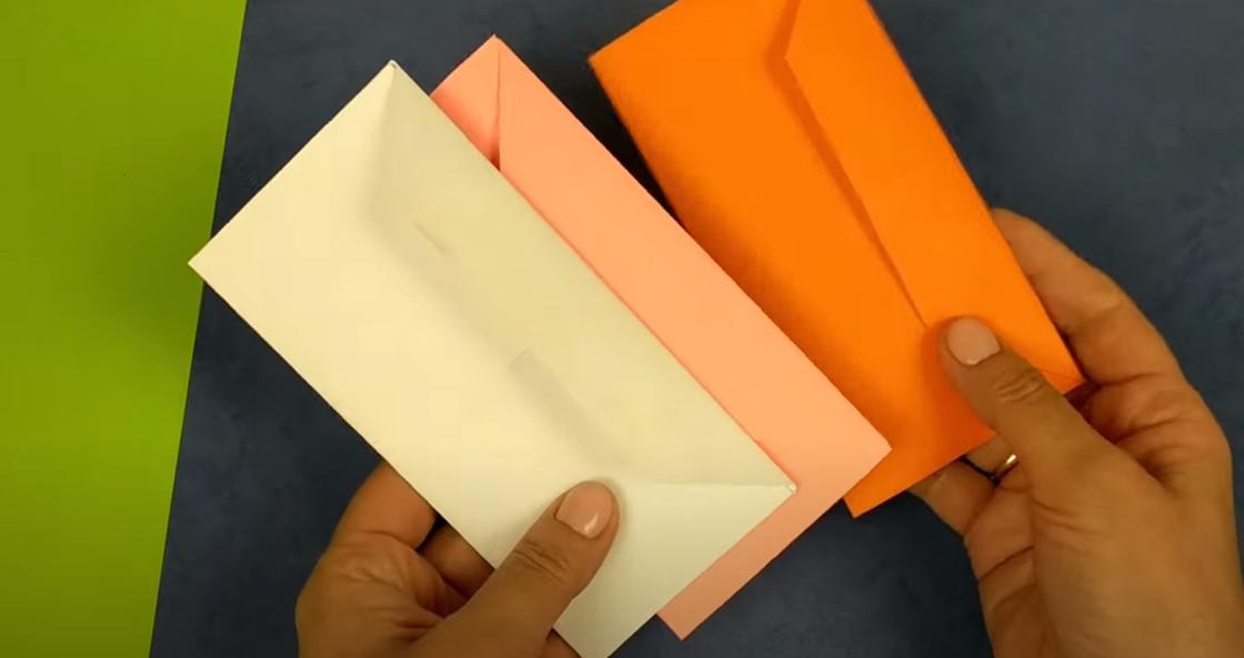 В руках держат три разноцветных конверта с прямоугольным сгибом