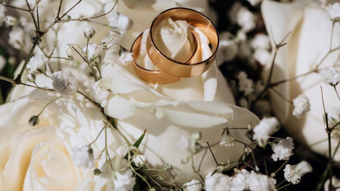 Два обручальных кольца лежат на подушечке, украшенной нежными белыми цветами