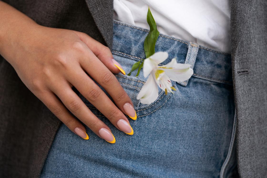 Женская рука с желтым френчем возле кармана джинсов