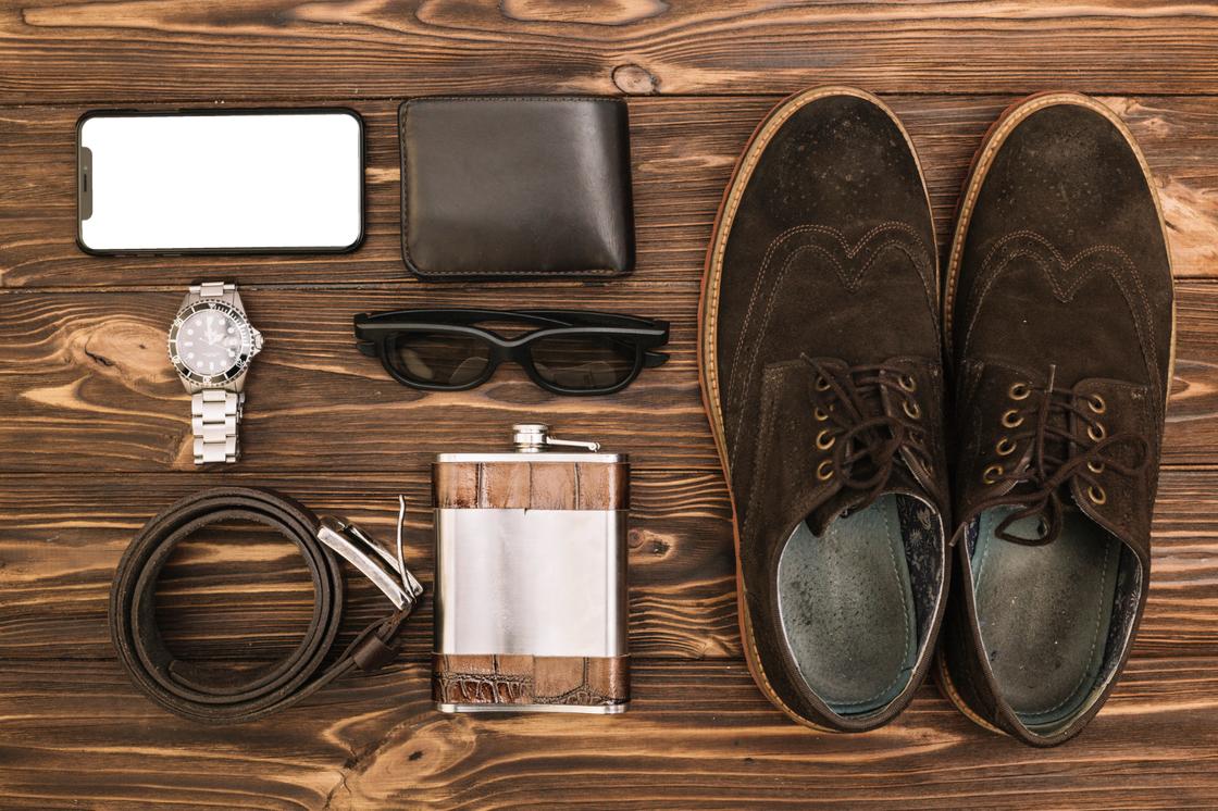 Рядом с ботинками кожаный ремень, фляга, очки, портмоне, часы, телефон
