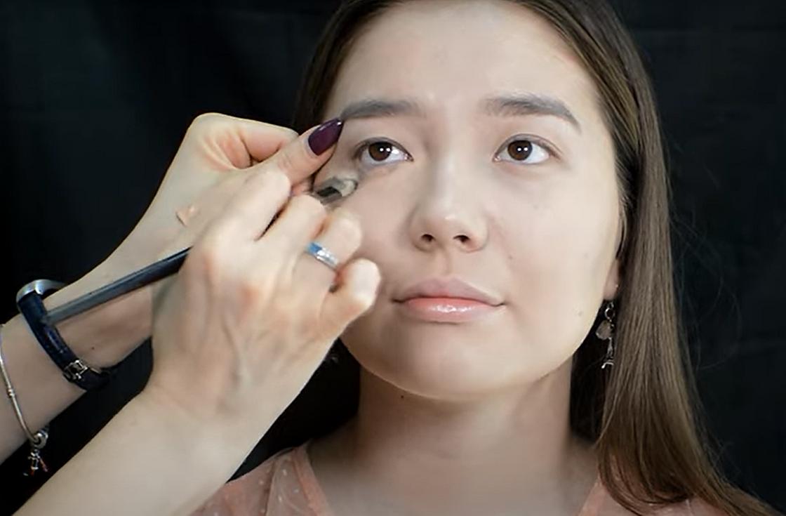 Женщина наносит консилер под глаза азиатской формы кисточкой