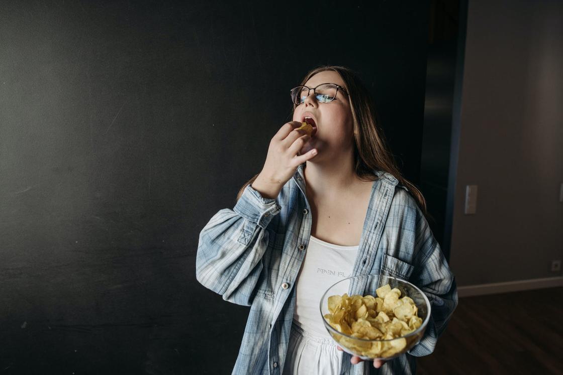 Девушка с полноватой фигурой ест чипсы из круглой миски