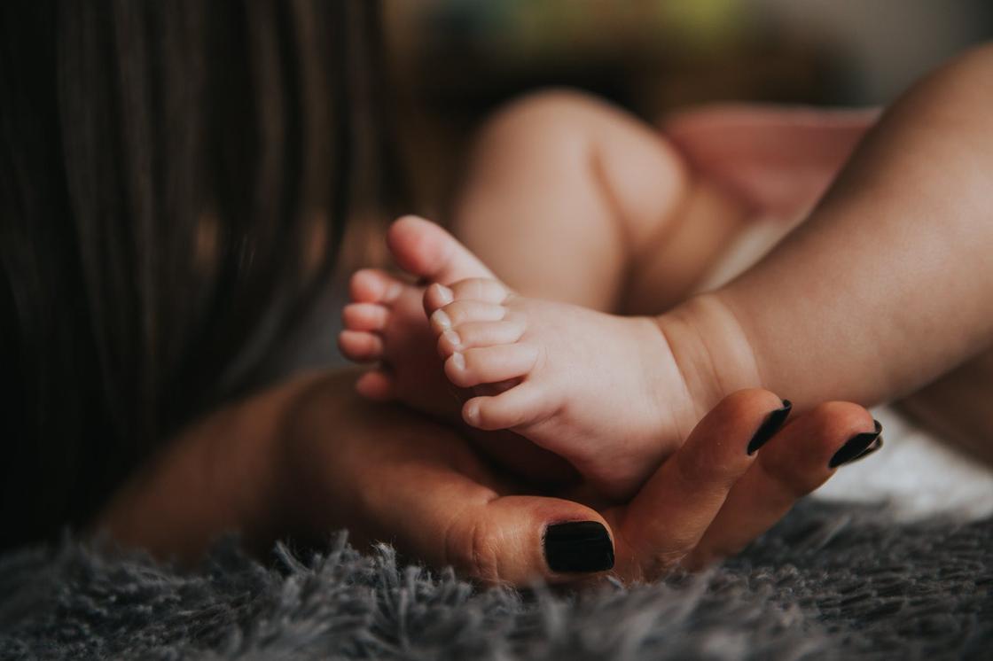 Женская рука держит ножки младенца