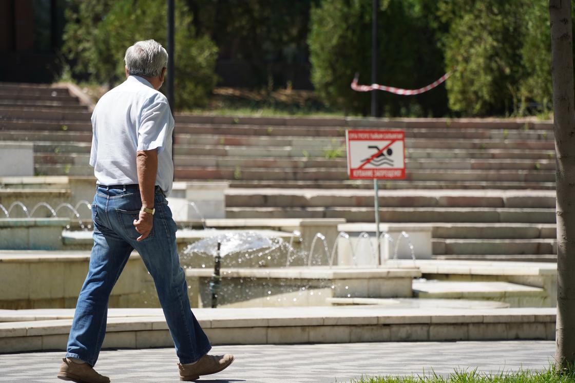 Мужчина идет мимо фонтана и знака о запрете купания