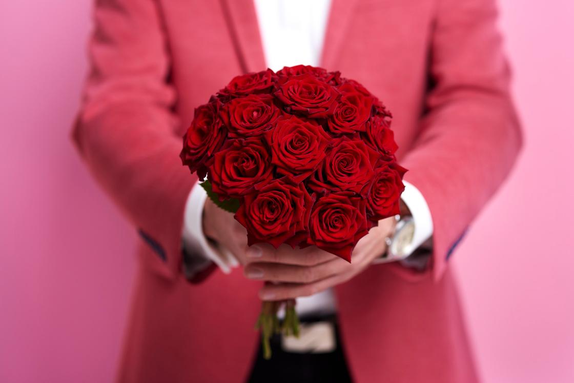 Мужчина в красном пиджаке протягивает руки с букетом красных роз
