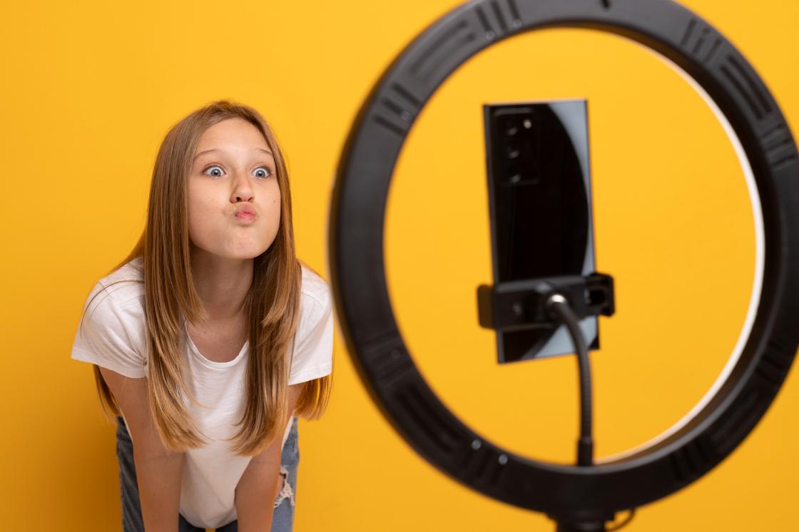 Девочка смотрит в камеру телефона, закрепленного на штативе с лампой