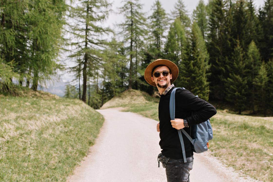 Мужчина с рюкзаком стоит посреди лесной дороги