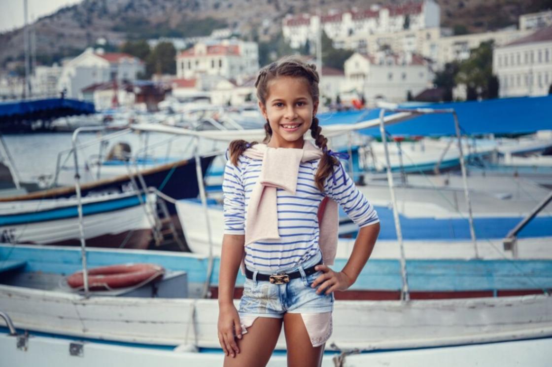 Девочка стоит на фоне залива и лодок