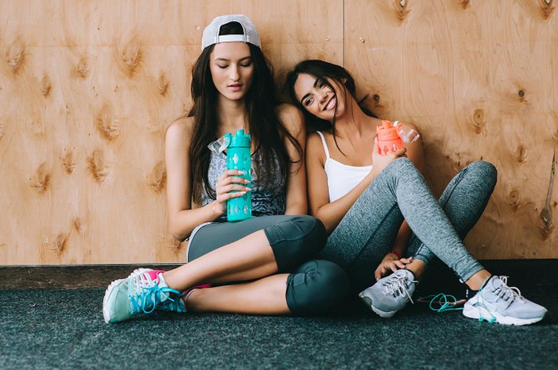 Две девушки с бутылками воды в одежде для фитнеса