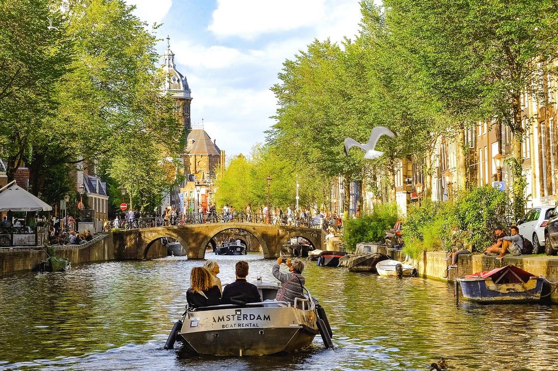 Лодка с туристами идет по водному каналу в Амстердаме