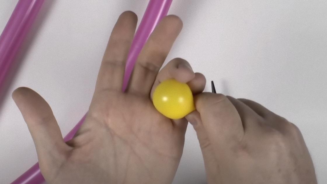 Желтый надутый шарик держат в пальцах