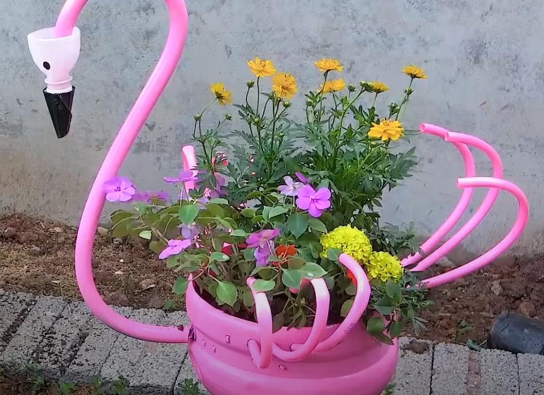 Клумба из пластиковых деталей в виде розового фламинго. В емкости растут бархатцы и другие цветы