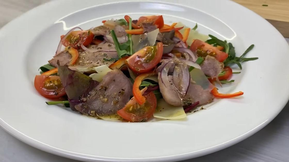 На сервировочной тарелке салат из помидоров, лука, сладкого перца и сваренного свиного языка