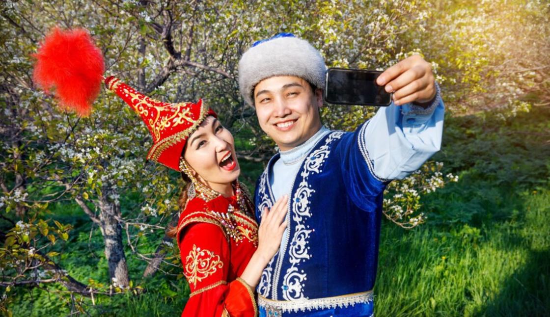 Казахи в национальных костюмах делают селфи на фоне цветущих деревьев