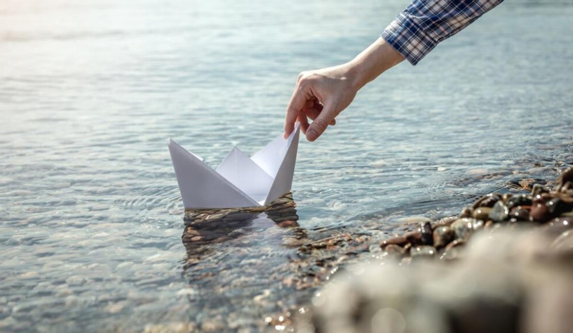 Мужчина пускает по воде бумажный кораблик