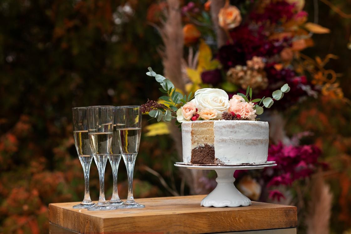 Торт, декорированный живыми цветами на столе с бокалами шампанского