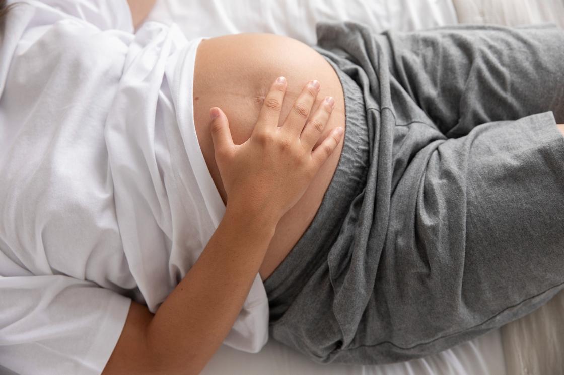Беременная женщина держит рукой живот