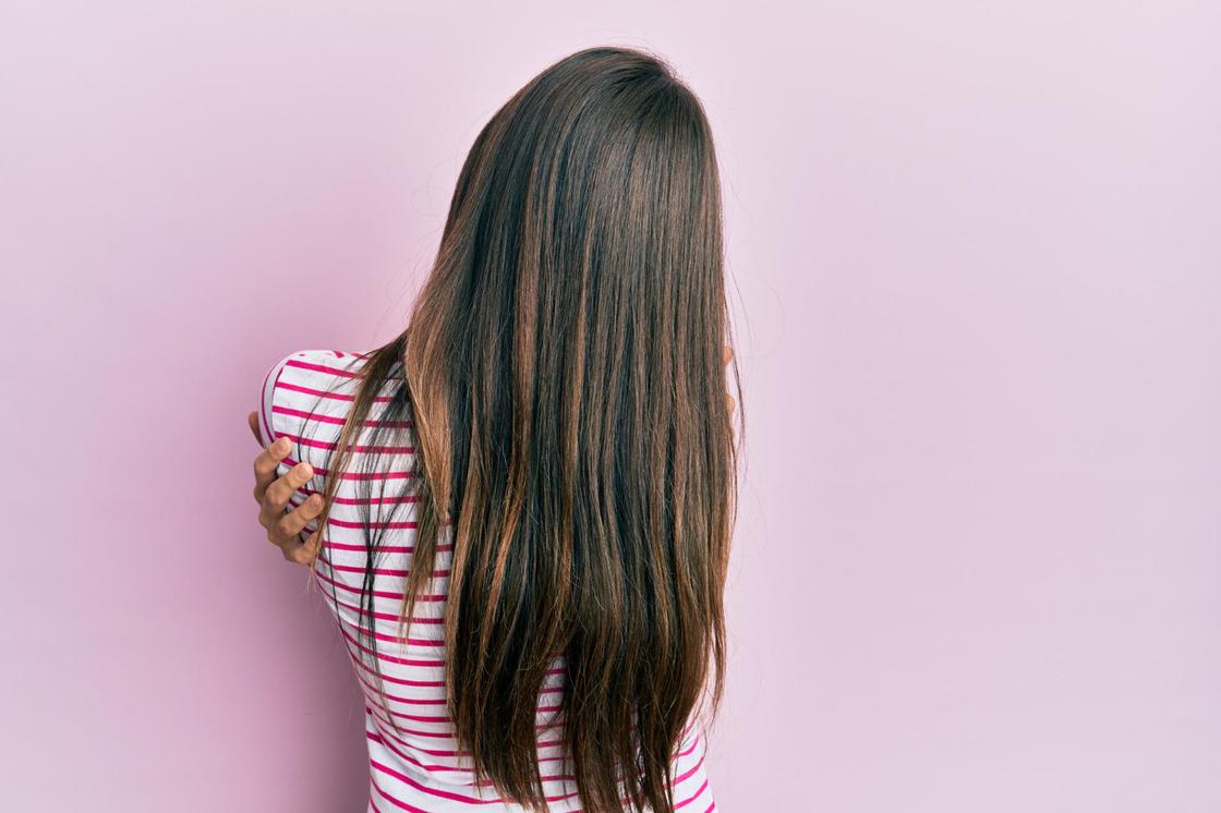 Девушка с мелированием на темных волосах стоит спиной