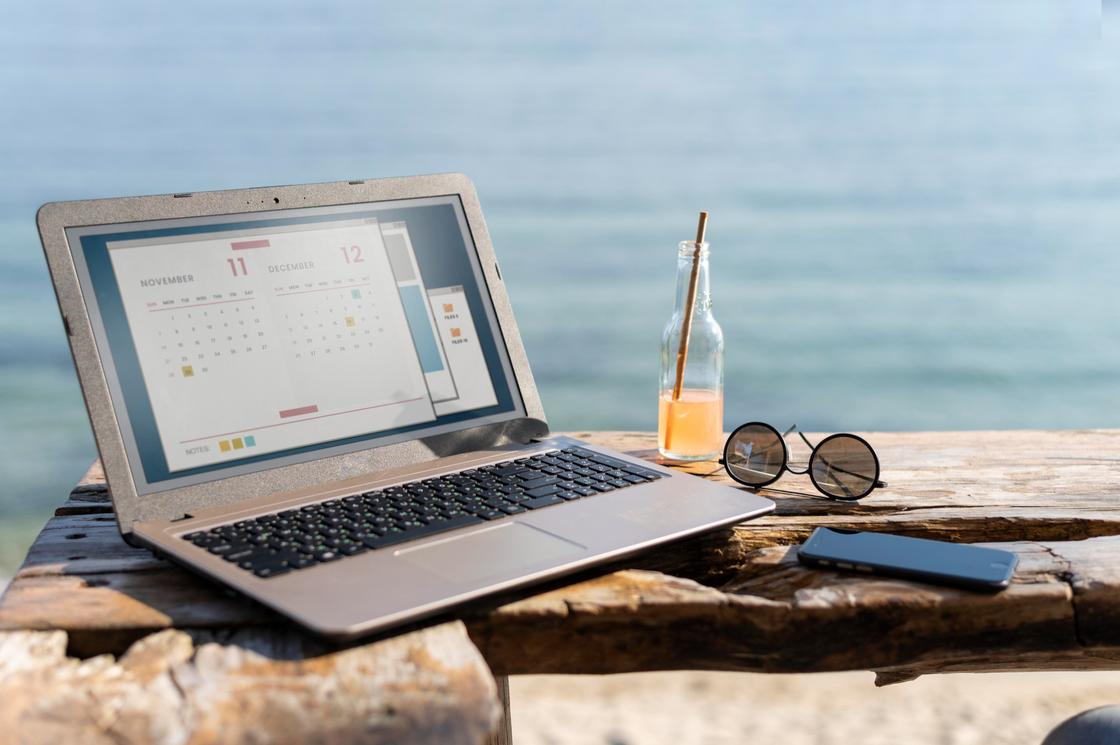 На фоне моря ноутбук, очки, телефон и бутылка