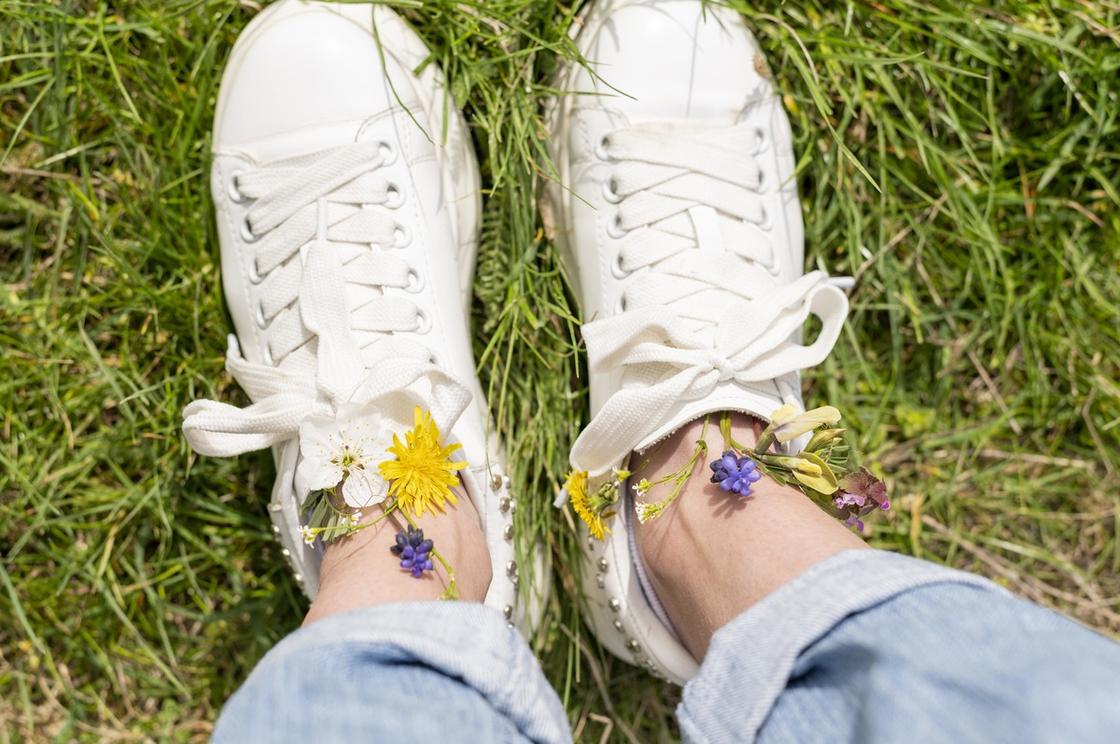 Ноги в белых кроссовках на траве. С кроссовок торчат полевые цветы