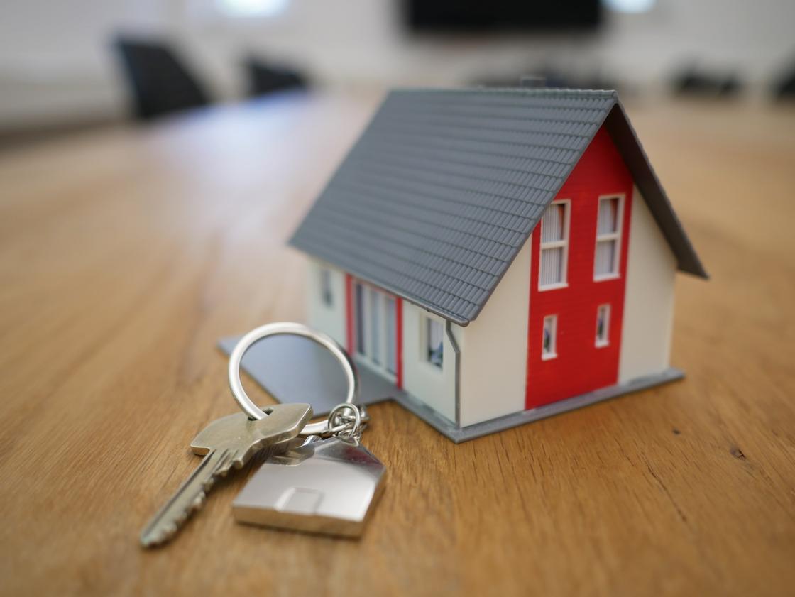 На столе стоит красный макет дома и лежит связка ключей