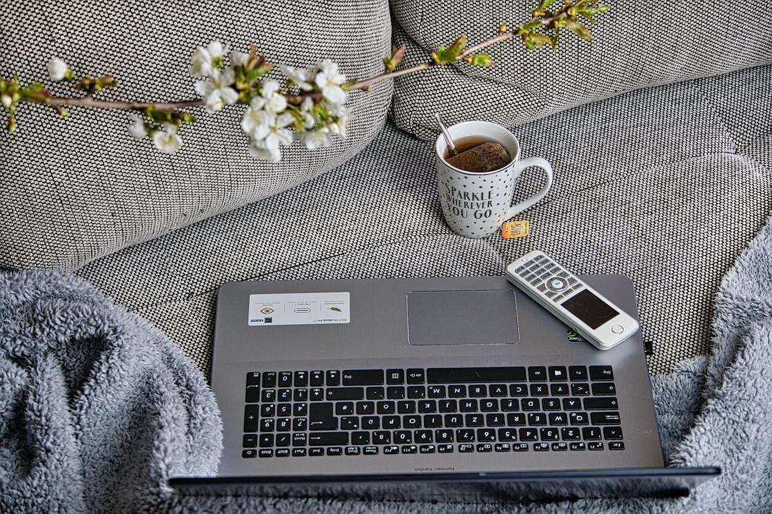 На диване стоит чашка чая, лежит ноутбук и телефон