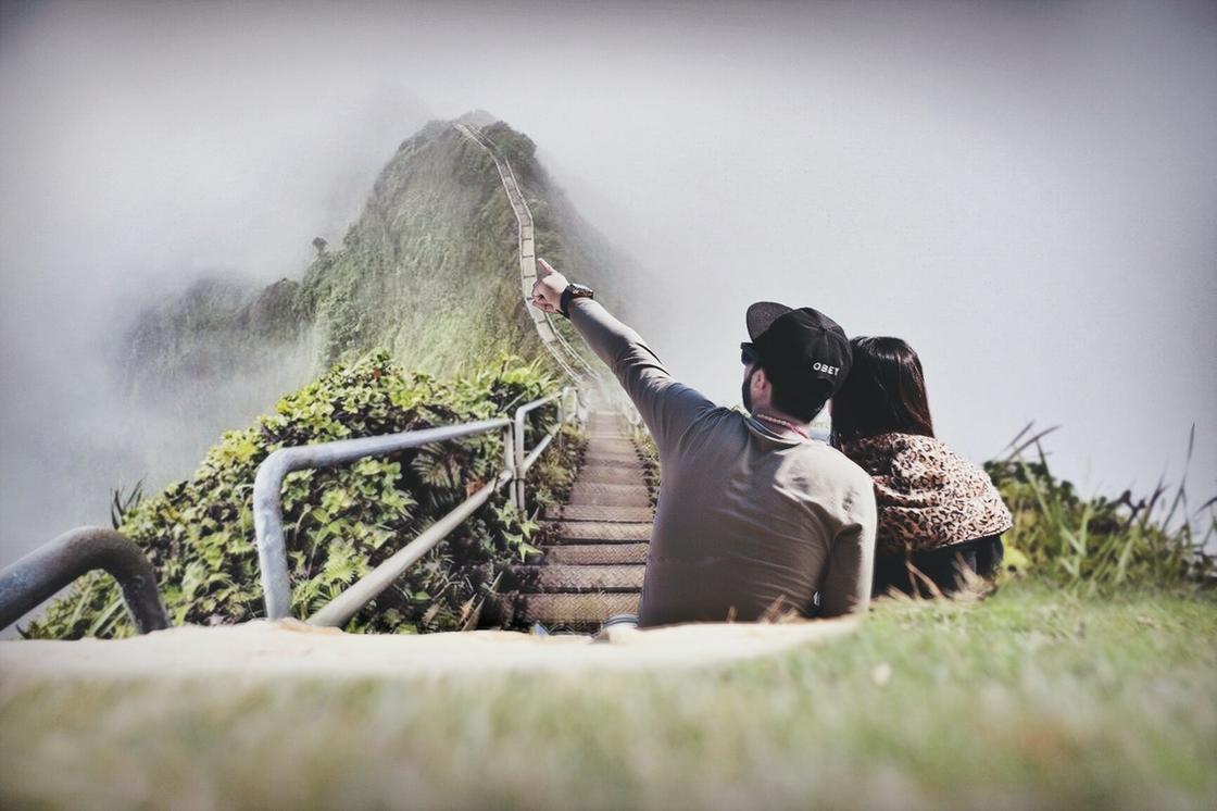 Парень и девушка сидят, обнявшись и глядя на горы