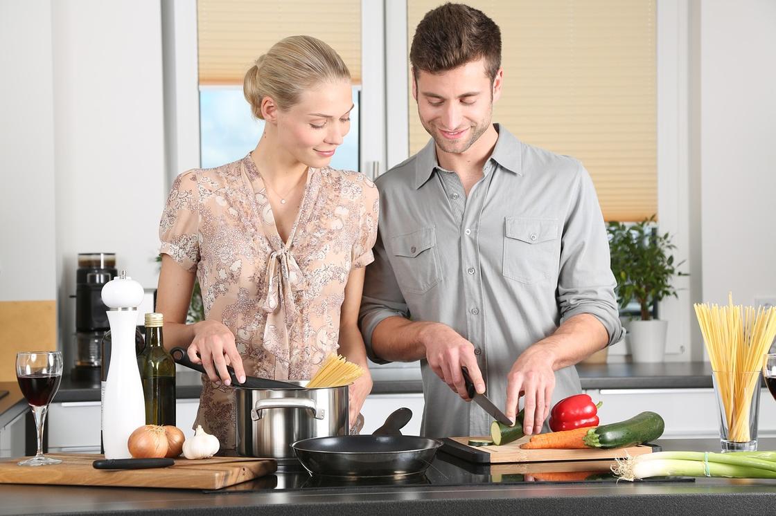 Парень и девушка готовят пасту и нарезают овощи