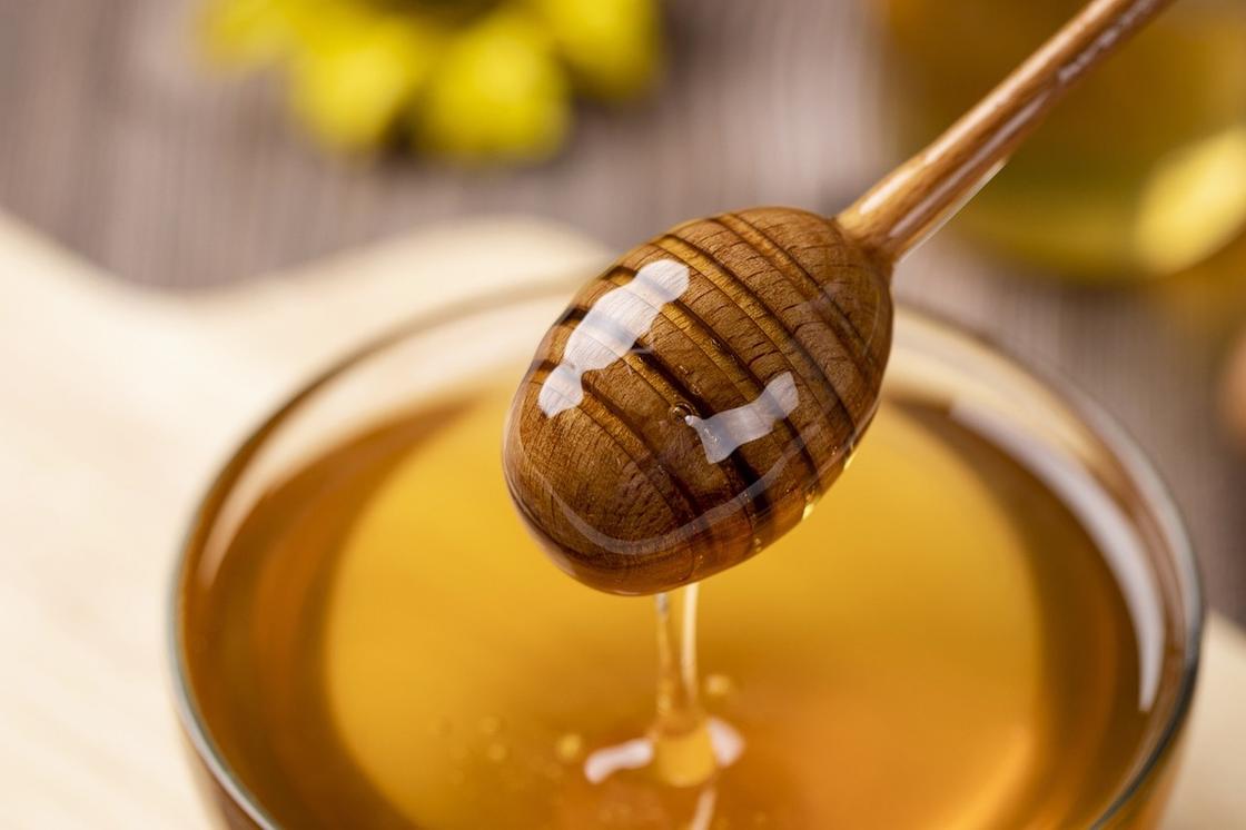 Жидкий светлый мед в миске набирают деревянной палочкой для меда