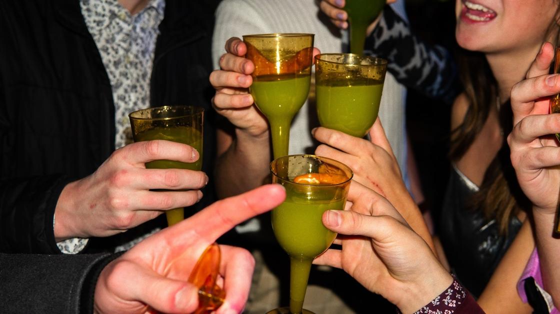 Люди в руках держат бокалы с зеленым коктейлем