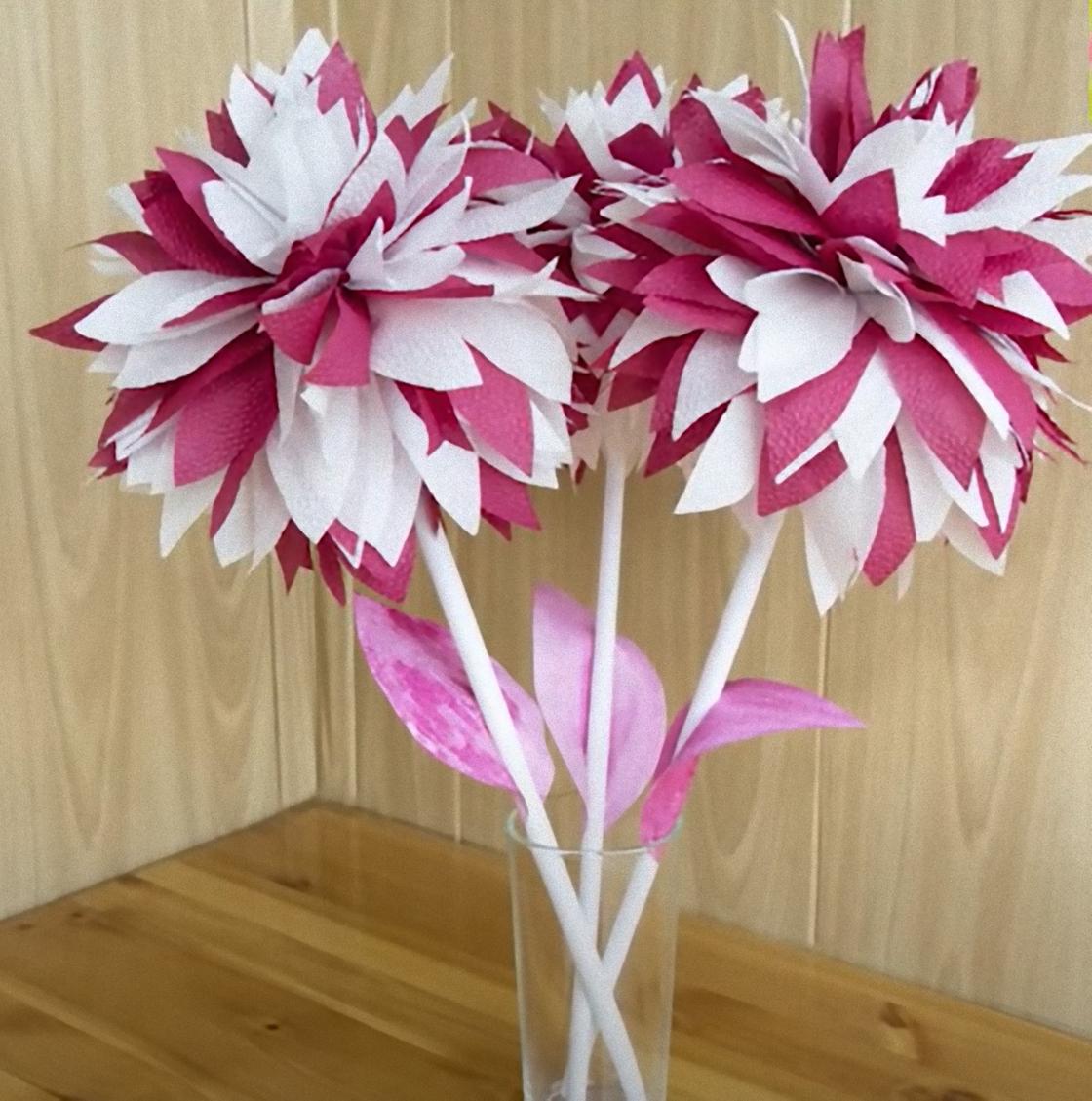 Двухцветные бумажные цветы из салфеток стоят в стекляннной вазе на столе.