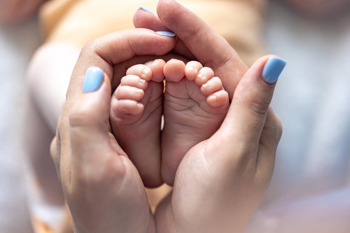 Женские руки держат ножки младенца