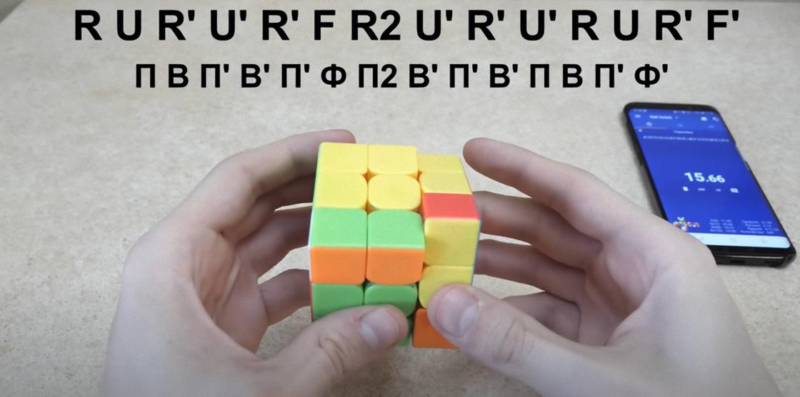 На кубике Рубика выполняют полную сборку по алгоритму «Т». Сверху записаны обозначения алгоритма