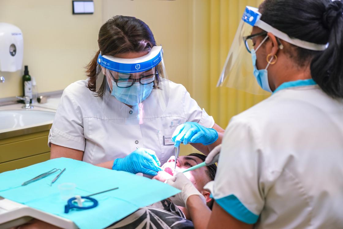 Женщина-стоматолог и медсестра работают медицинскими инструментами на зубах мужчины