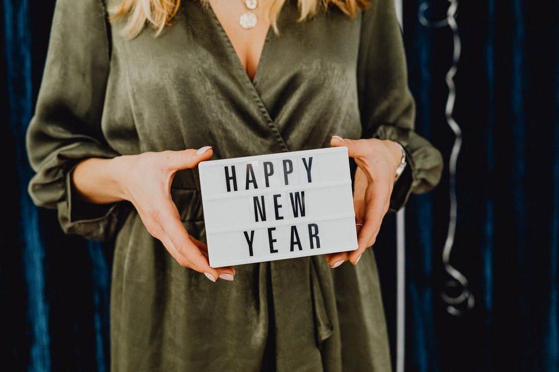 Женщина в зеленом платье держит табличку с английской надписью "Happy New Year" Женщина в зеленом платье держит табличку с английской надписью "Happy New Year"