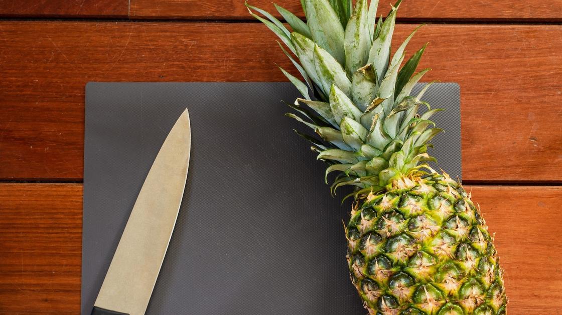 Нож и спелый ананас на дощечке