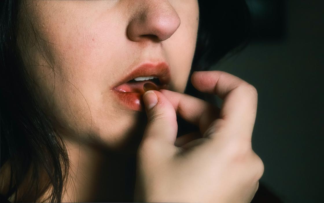 Девушка кладет таблетку себе в рот