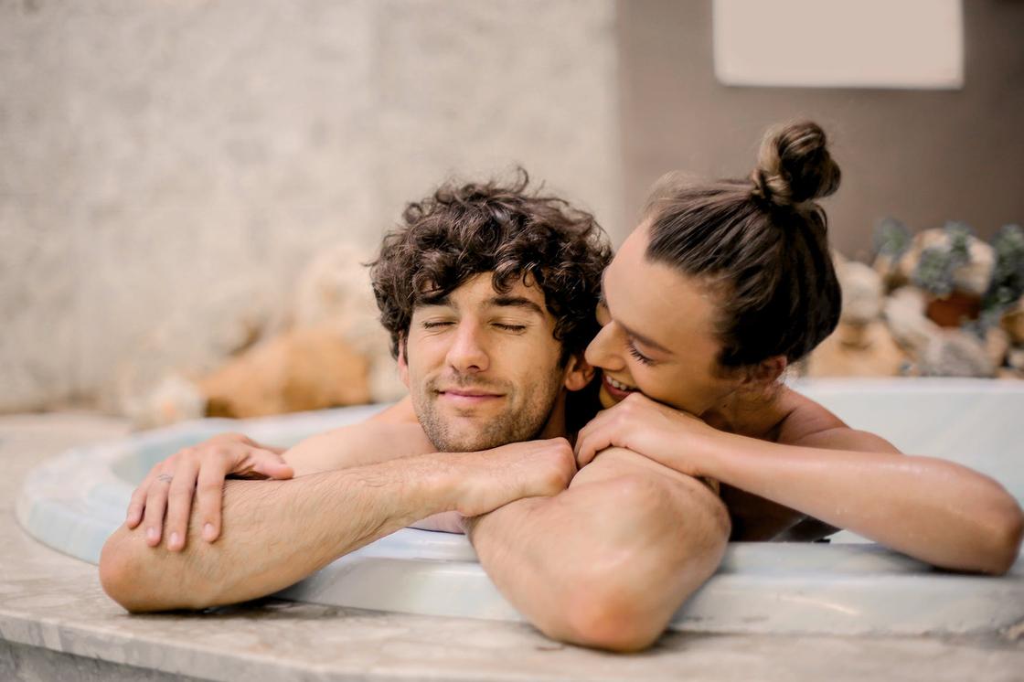 Девушка сидит в ванной, обнимая мужчину за плечи и наклоняясь к его уху