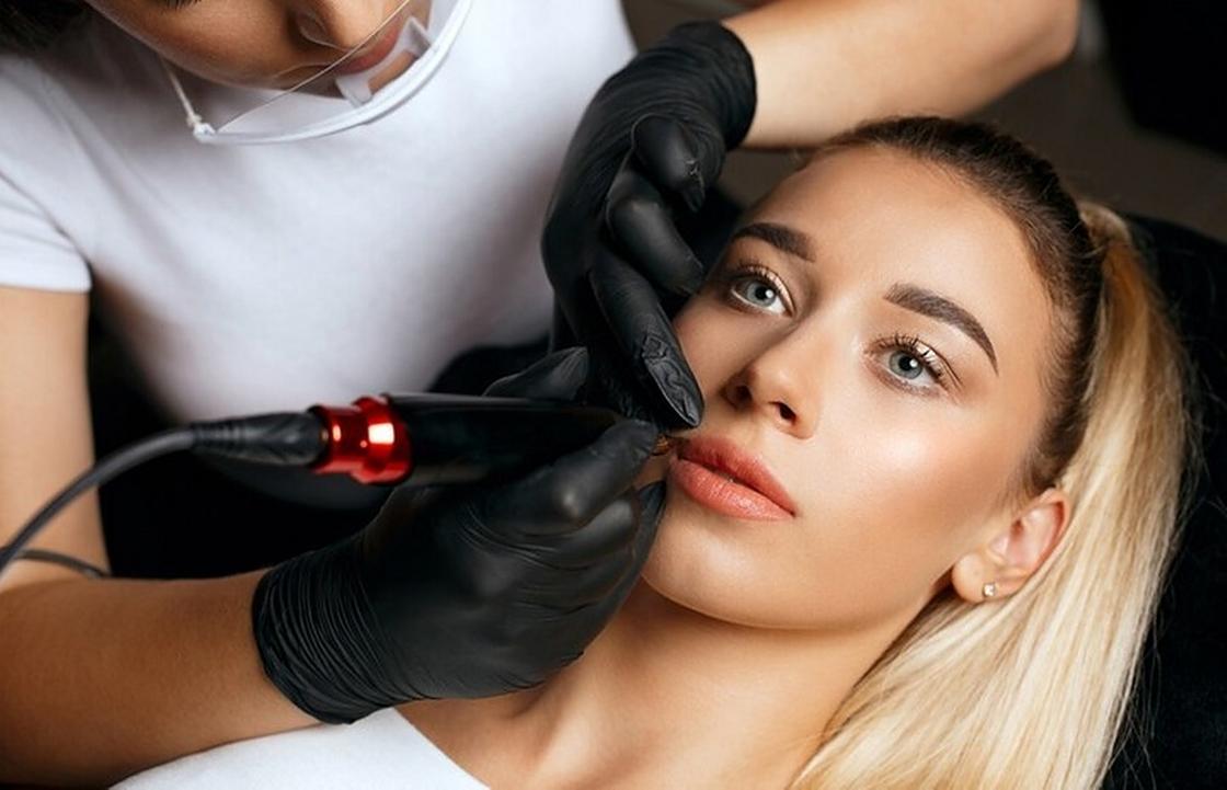 Девушке мастер делает перманентный макияж губ в салоне