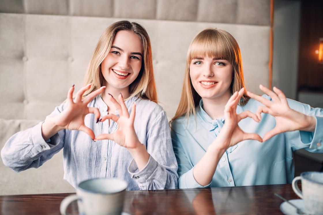 Две девушки в кафе показывают руками сердца