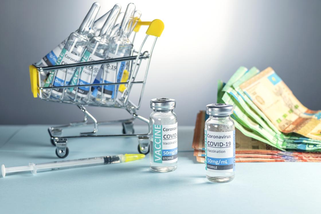 Вакцины от коронавируса стоят на столе рядом с купюрами тенге