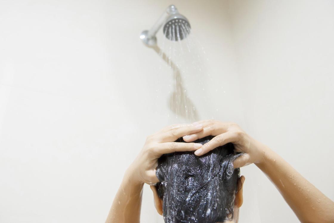 Девушка под душем смывает кондиционер для волос