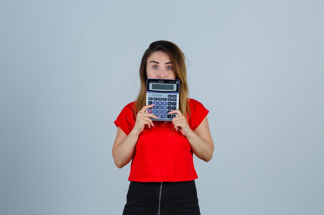 Девушка в красной футболке держит перед лицом калькулятор