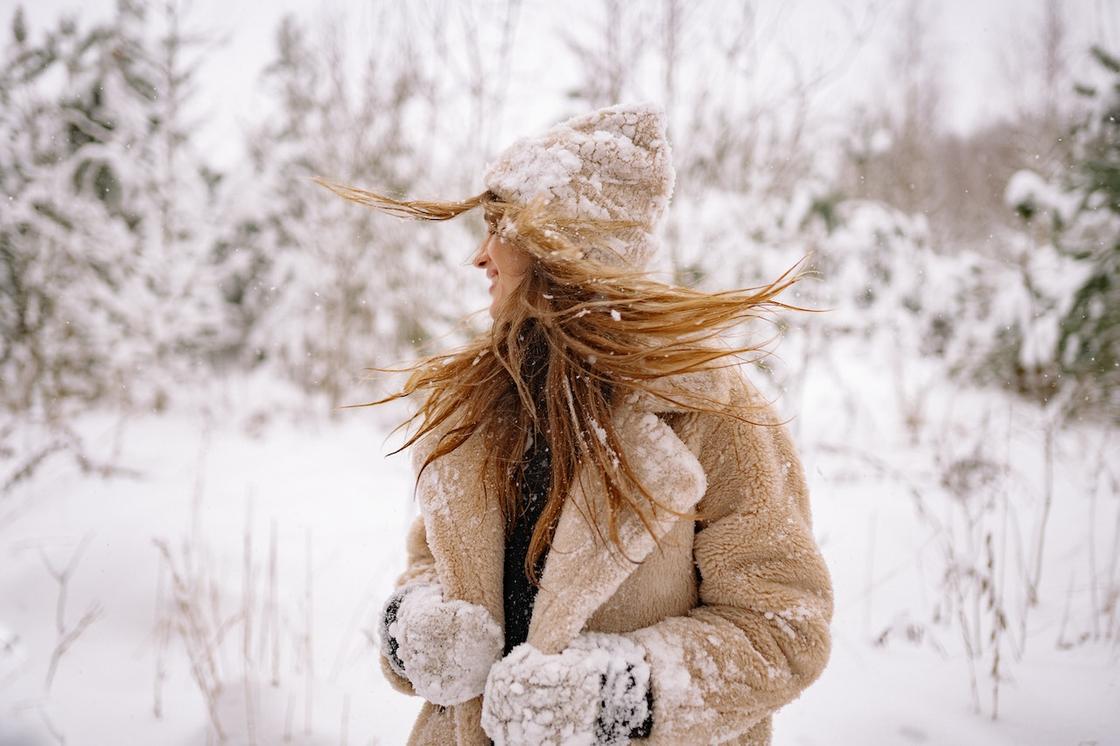 Девушка с длинными волосами в шубе и шапке в лесу зимой