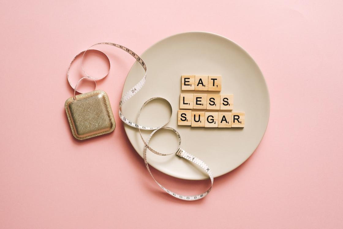 Выложенная из букв надпись на английском языке "ешь меньше сахара" на тарелке рядом с метром